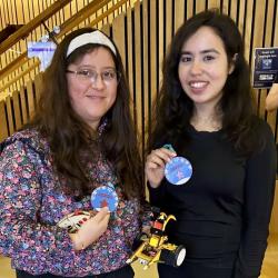 Two women holding blue medals and smiling at the camera while holding a small remote controlled robot