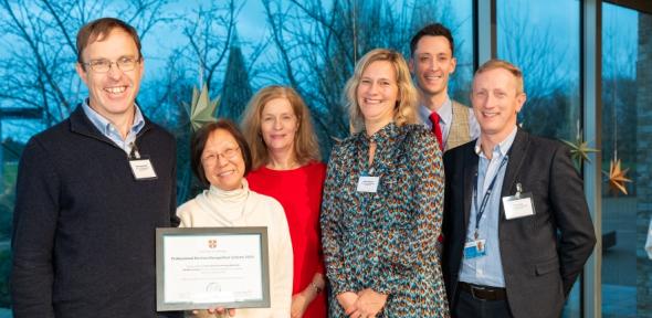 Group of six people, three men and three women, smiling at the camera in professional clothing holding a certificate